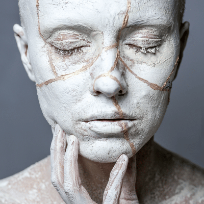 das Gesicht einer Frau, das Brüche und Bruchstellen im Gesicht zeigt. Diese sind mit Gold aufgefüllt. Kintsugi als Symbol für die Heilung bei Menschen